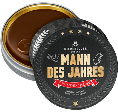 Eine schwarze, runde Verpackung mit der Aufschrift “Mann des Jahres Heldentaler”, in der Dose ein großer Schokoladentaler