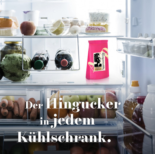 Zu sehen ist ein geöffneter Kühlschrank mit allerlei Gemüse, Obst und Getränken. Im mittleren Fach steht rechts ein pink verpacktes Stück Käse mit dem Appenzellerin-Motiv.