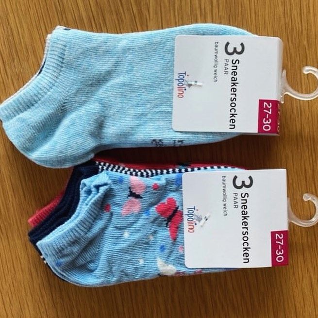 Zu sehen sind 2 Pack Sneakersocken mit Verpackung. Oben liegt ein Pack mit 3 Paar Socken in Gr. 27-30, man sieht von oben einen hellblauen Socken. Unterhalb liegt ein weiteres Pack mit 3 Paar Sneakersocken der Gr. 27-30, die sind jedoch kürzer und kleiner.