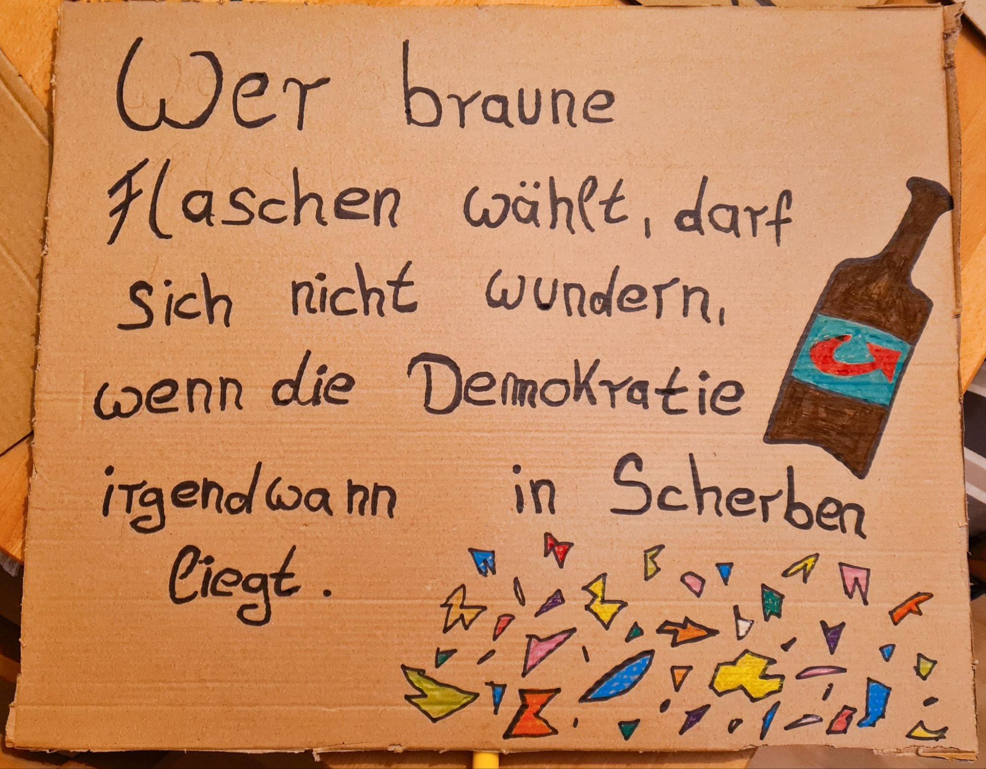 Foto von einem Demoplakat. In schwarzer Schrift steht darauf: Wer braune Flaschen wählt, darf sich nicht wundern, wenn die Demokratie irgendwann in Scherben liegt. An der rechten Seite ist eine braune Flasche mit noAfd-Logo gemalt, unten drunter bunte Scherben.