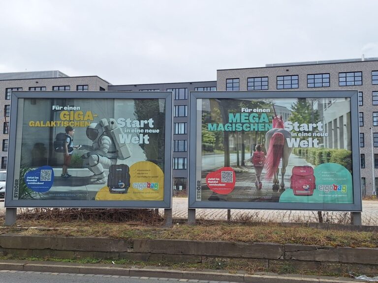 Zwei große Werbeplakate von ergobag. Auf einem ein Junge mit blauem Ranzen, welcher einer/einem Astronaten/ Astronautin die Hand gibt. Auf dem anderen Plakat ein Mädchen, welches mit einem pinken Ranzen neben einem Einhorn läuft.