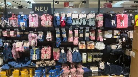 Nahaufnahme eines Regals mit Herbstmode für Kinder in rosa und blau. Geblümte Motive auf den Rosa Sachen und Autos auf den blauen.