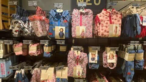 Foto eines Verkaufsregal in dem Kinderkleidung hängt. Kinderjacken, Trinkflaschen und Halstücher. Es gibt eine Auswahl an Kinderjacken, Trinkflaschen und Halstüchern in rosa mit Blumen oder Blau mit Autos.