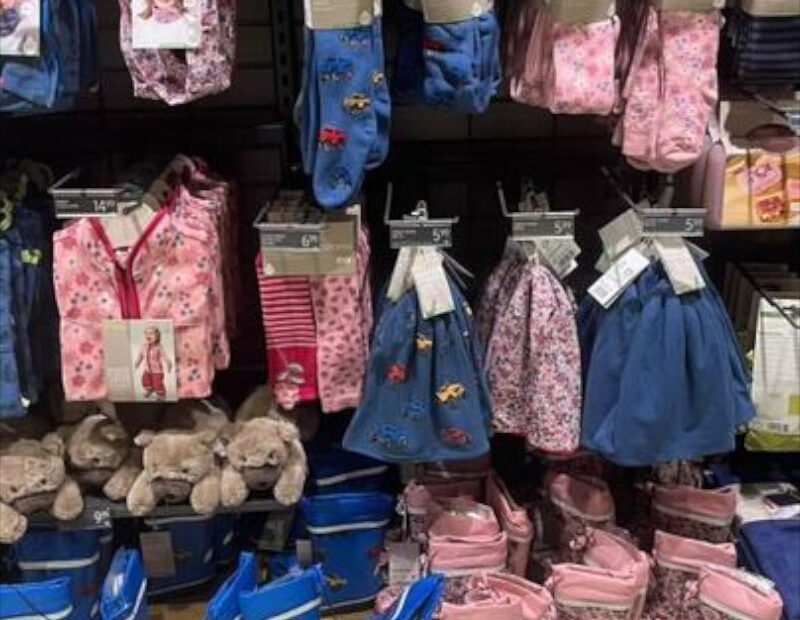 Nahaufnahme eines Regals mit Herbstmode für Kinder in rosa und blau. Geblümte Motive auf den Rosa Sachen und Autos auf den blauen.