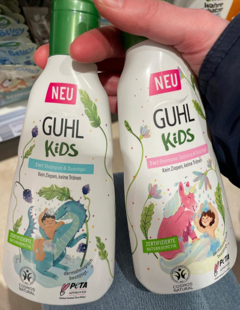 Zwei weiße Flaschen Guhl Kids werden nebeneinander in einer Hand gehalten. Links steht ein 2in1 Shampoo & Duschgel mit türkisfarbenem Schriftfeld, Brombeeren und einem blau-grünen Drachen. Rechts steht ein 3in1 Shampoo, Spülung & Duschgel mit rosa Schriftfeld sowie einem rosafarbenen Einhorn mit pastellfarbener Mähne. Auf beiden Flaschen sind Kinderfiguren abgebildet.